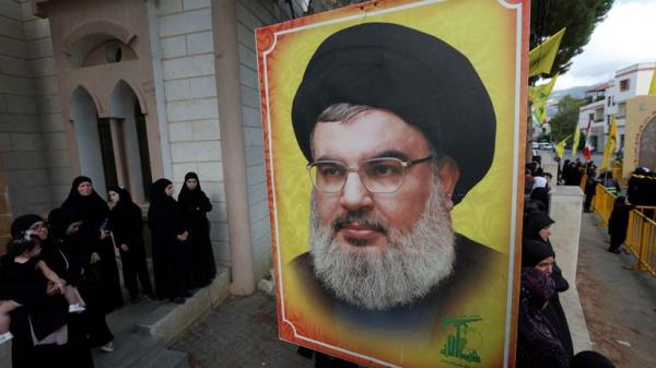 People stand near a picture of Hezbollah leader Sayyed Hassan Nasrallah during the funeral of Hezbollah member Ali Mohamed Chalbi, after hand-held radios and pagers used by Hezbollah deto<em></em>nated across Lebanon, in Kfar Melki, Lebanon September 19, 2024. REUTERS/Aziz Taher