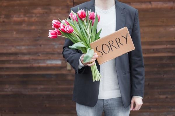 A man holding flowers and a 'sorry' sign